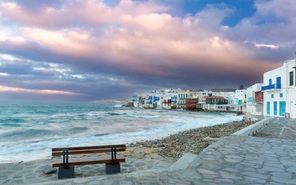 Little Venice is one of the most charming neighborhoods in Mykonos Town, where colorful houses are built right on the water's edge. It is a vibrant hub of cafes and bars, perfect for enjoying a drink while the waves crash below. With the famous Mykonos windmills as a backdrop, it offers a quintessential island experience, blending historic maritime charm with a lively and cosmopolitan social scene.