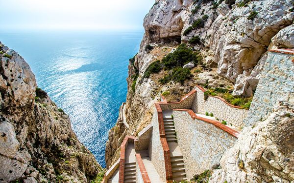 Neptune’s Grotto is a spectacular stalactite sea cave located on the cliffs of Capo Caccia. Visitors can reach it by boat or by descending the "Escala del Cabirol," a 654-step staircase carved into the rock. Inside, the massive chambers and the subterranean saltwater lake create a magical and awe-inspiring natural gallery, showcasing the incredible geological wonders of Sardinia’s coastline.